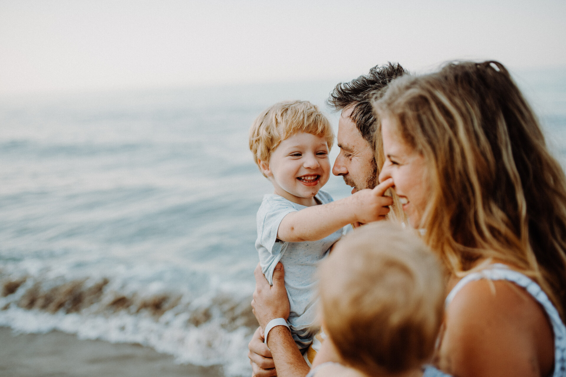 A young family with two toddler children standing on beach on summer holiday, laughing.